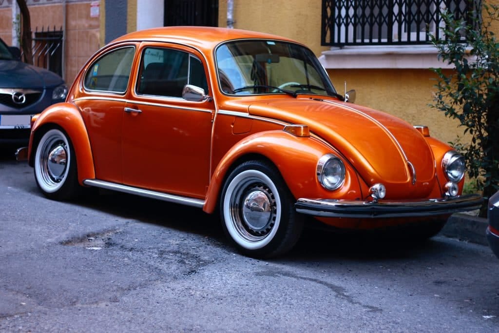 An orange volkswagen beetle parked on the side of a street.