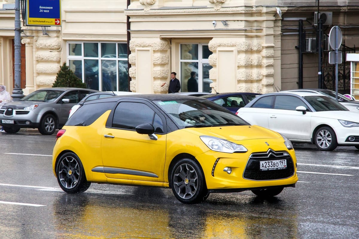 A yellow car driving down the street in the rain.