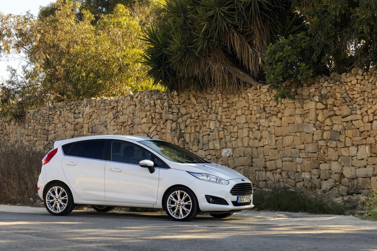 A white ford fiesta parked in front of a stone wall.