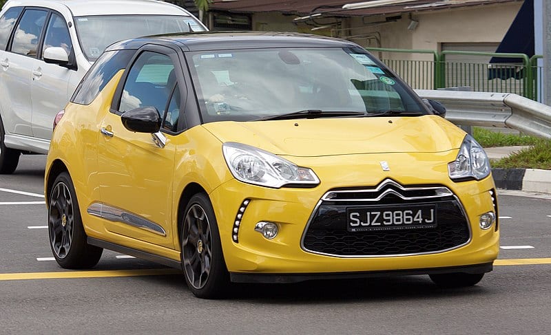 A yellow citroen c3 is driving down the street.