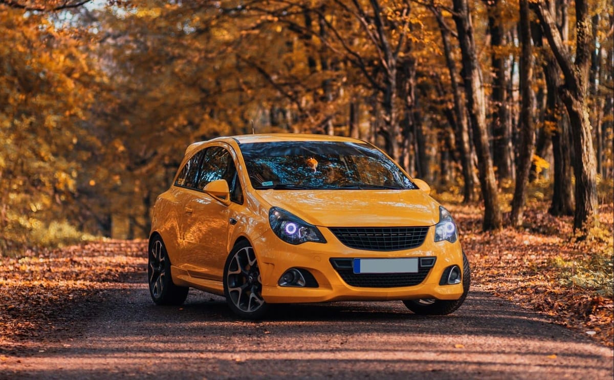 A yellow car is driving down a road in the autumn.