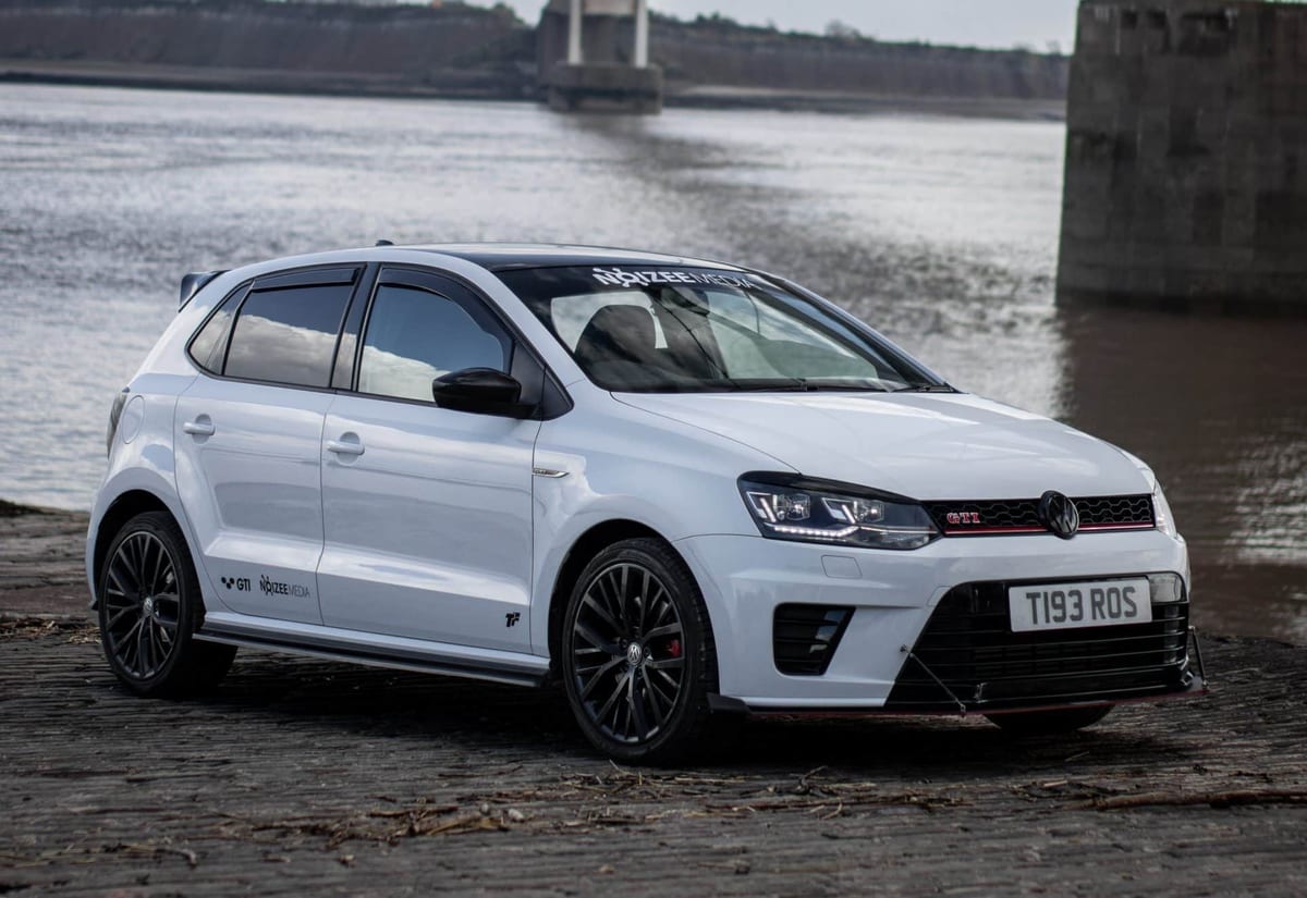 A white volkswagen polo parked on the side of a river.